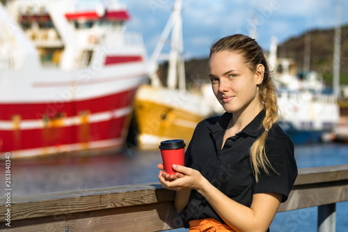 A young female waitress holding a disponsable paper cup of coffee looking camera outdoors. photo