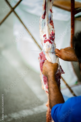 The process of cutting the meat during Hari Raya. A man with a knife is cuttting the meat hanging on the hook.