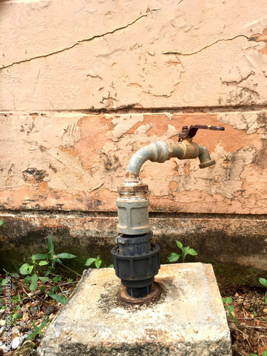 Close up old rusty iron faucet besid old cement wall in garden.