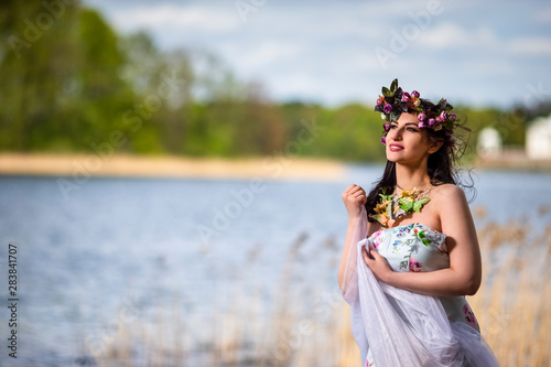 Gorgeous Caucasian Brunette Woman in Decorated Dress and Flowery Chaplet with Butterflies. Posing Against Nature Background photo