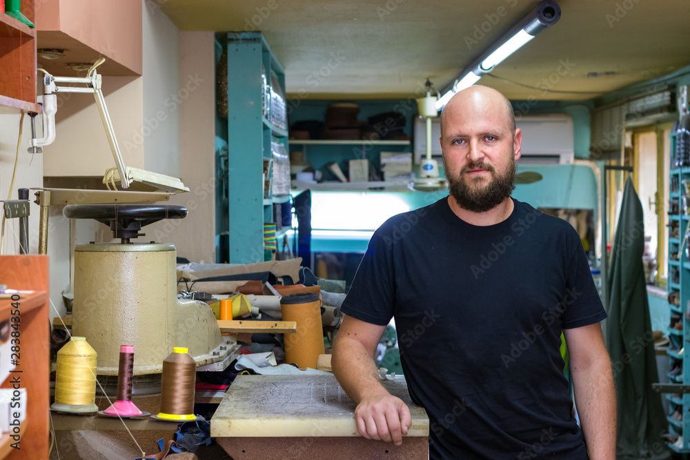 Portrait of a shoemaker bald man with beard, posing standing at his workshop. Portrait of a shoemaker bald man with beard, posing standing at his workshop.