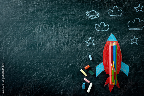 Education or back to school Concept. Top view of Painted paper rocket with colorful of color pencil and chalk on chalkboard background. Flat lay.