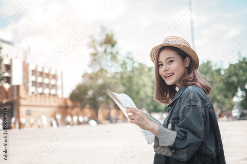 Smiling woman traveler in thapae gate landmark chiangmai thailand with backpack holding world map on holiday, relaxation concept, travel concept photo