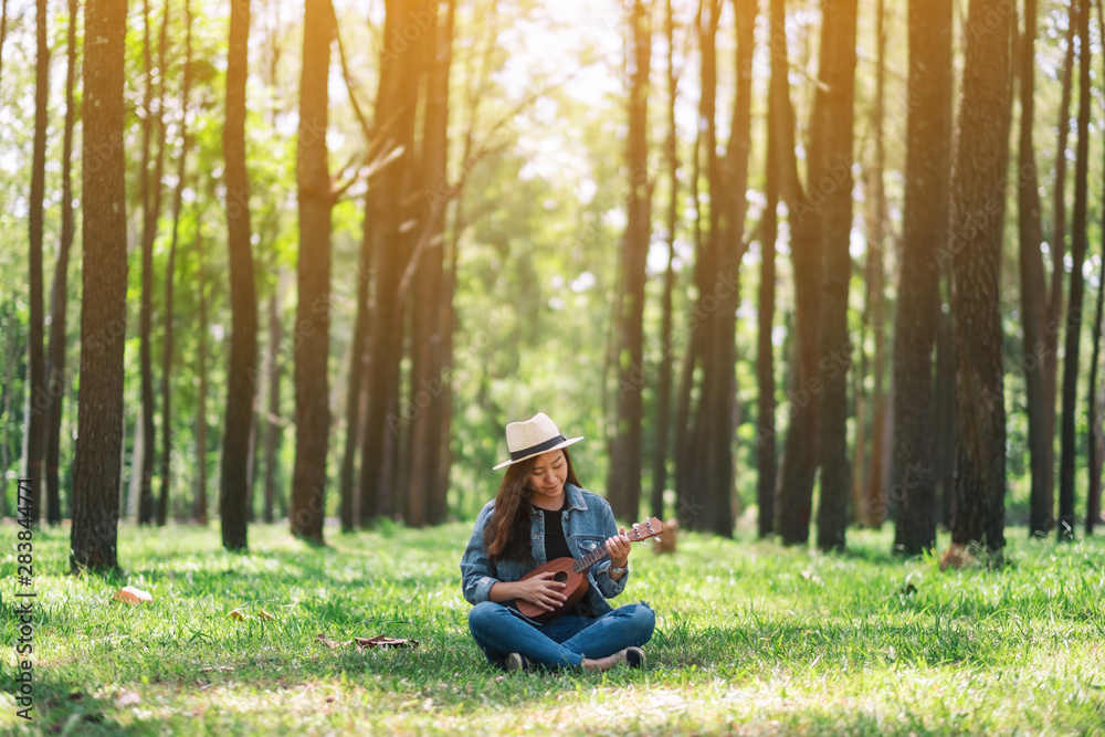 A beautiful asian woman sitting and playing ukulele in the park