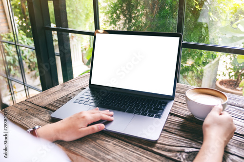 Mockup image of a hand using and touching on laptop touchpad with blank white desktop screen while drinking coffee photo