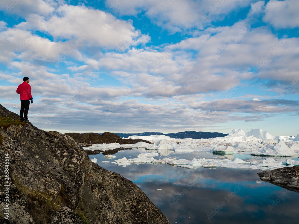 Global warming - Greenland Iceberg landscape of Ilulissat icefjord with giant icebergs. Icebergs from melting glacier. Arctic nature heavily affected by climate change. Person tourist looking at view