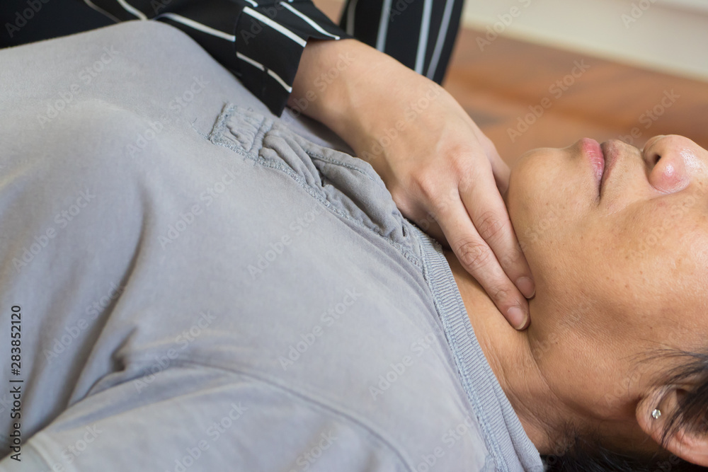 young woman doing CPR first aid, checking pulse to middle aged or senior unconscious woman; home first aid emergency rescue concept