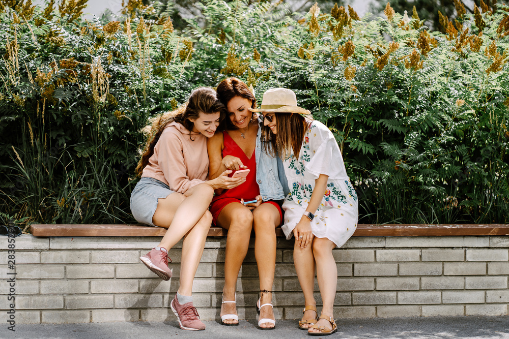 Naklejka premium Beautiful girls using a smart phone and smiling while standing outdoors