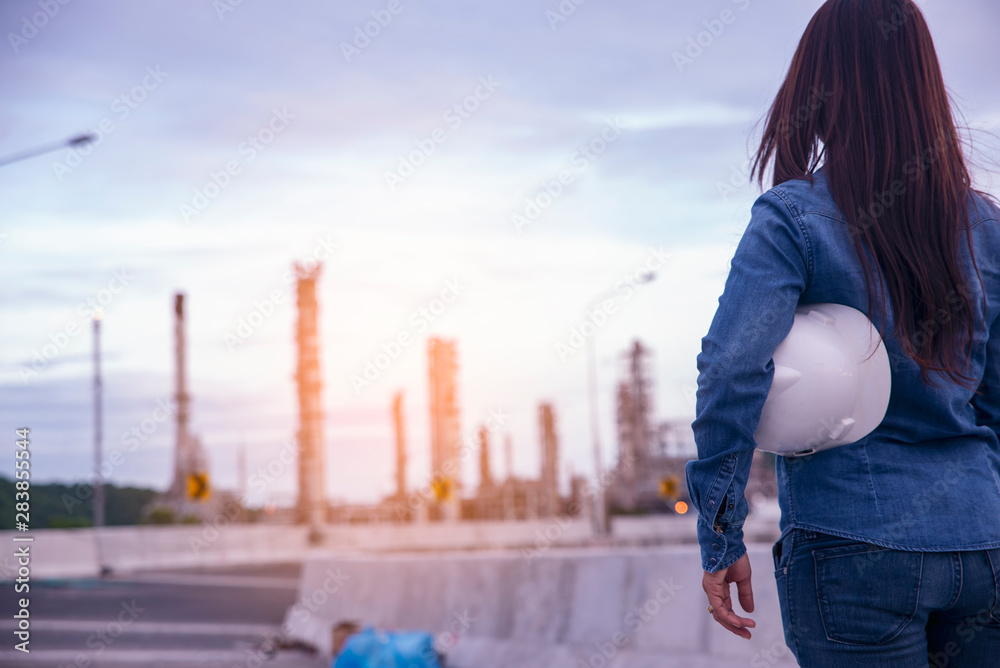 Woman Engineer and safety Officer concept.Young woman engineer wear safety hat (helmet) and blue jean.Safety Officer  inspector in front of refinery plant.