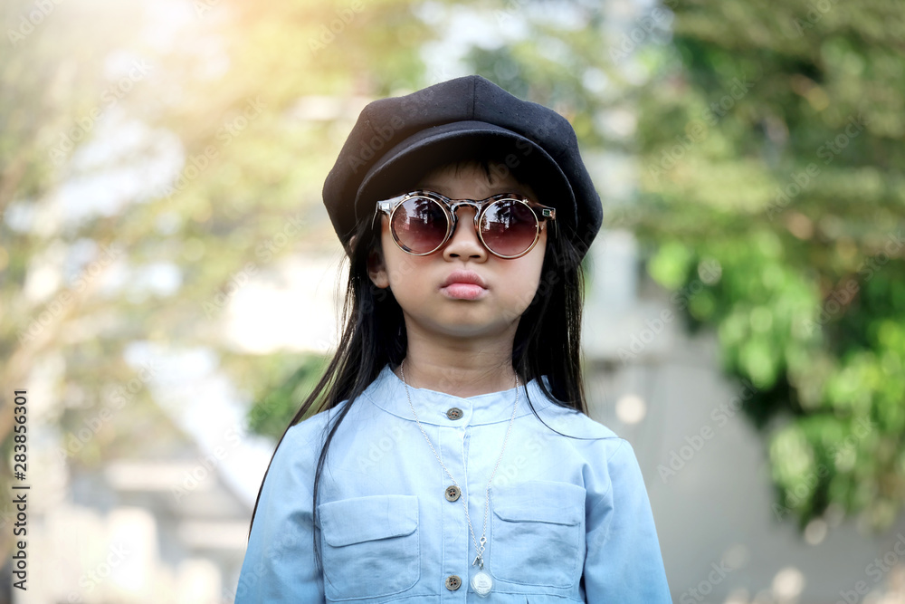 The Asian girl looks silently, wearing a denim shirt with sunglasses and a hat standing in the outdoor garden.