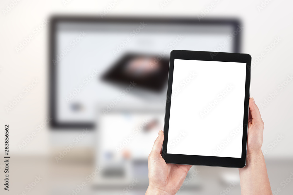 Mockup image of a woman holding a tablet and in the background a desktop computer with a laptop. Blank screen with copy space.
