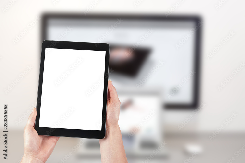 Mockup image of a woman holding a tablet and in the background a desktop computer with a laptop. Blank screen with copy space.