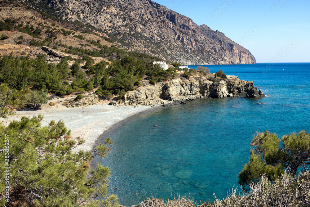 Vananda bay, pebble beach and crystal clear sea, above two small white chapels - Karpathos island, Aegean sea