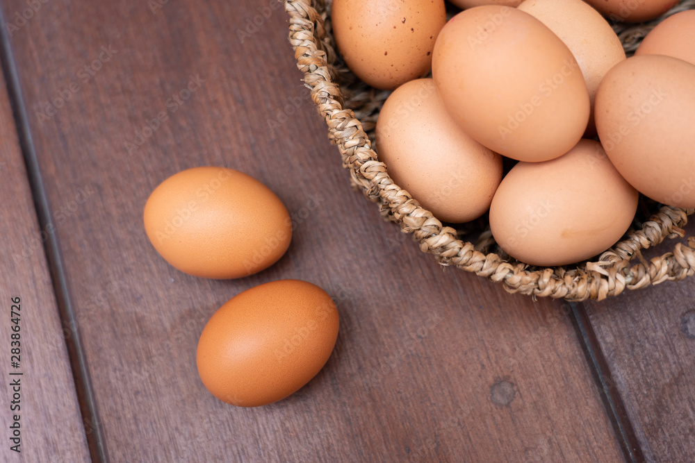 Close up of organic raw chicken eggs in bamboo basket with two eggs place on brown wooden floor background Close up of organic raw chicken eggs in bamboo basket with two eggs place on brown wooden floor background