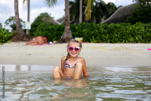 Little happy girl in sunglasses and a swimsuit in the sea. Concept of relaxation and vacation.