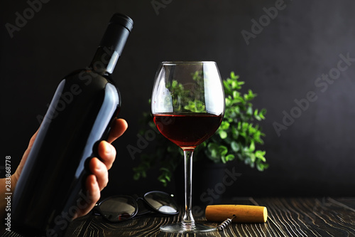 A glass of red dry wine on the table. Dark bottle and glass of wine.