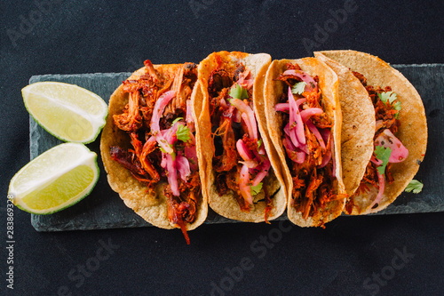 Mexican tacos top-view on a black background. Filled with cochinita pibil (shredded meat, onion and spicy), coriander and lime photo