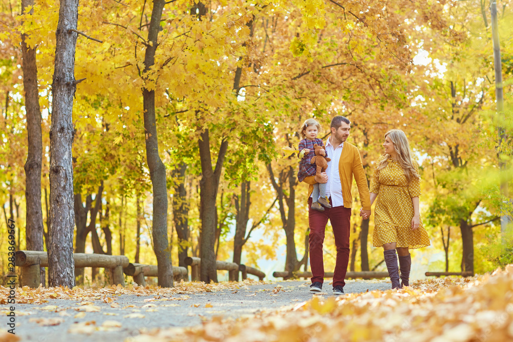 Obraz premium Family walking in the park in yellow autumn.