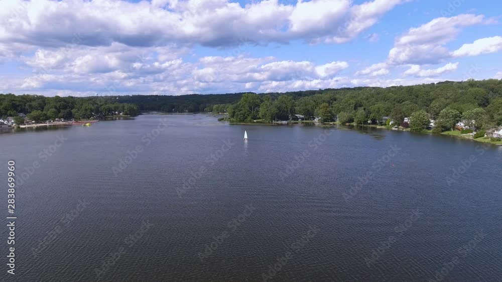 Aerial view of a small sailboat moving slowly alone on the beautiful lake in Northern New Jersey USA. Aerial view of a small sailboat moving slowly alone on the beautiful lake in Northern New Jersey USA.