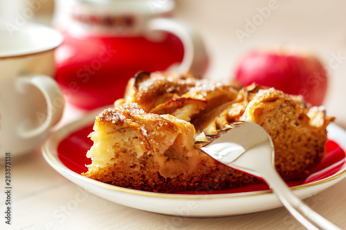 A piece of apple pie on the plate with fork, fresh apple and cup of coffee close up 