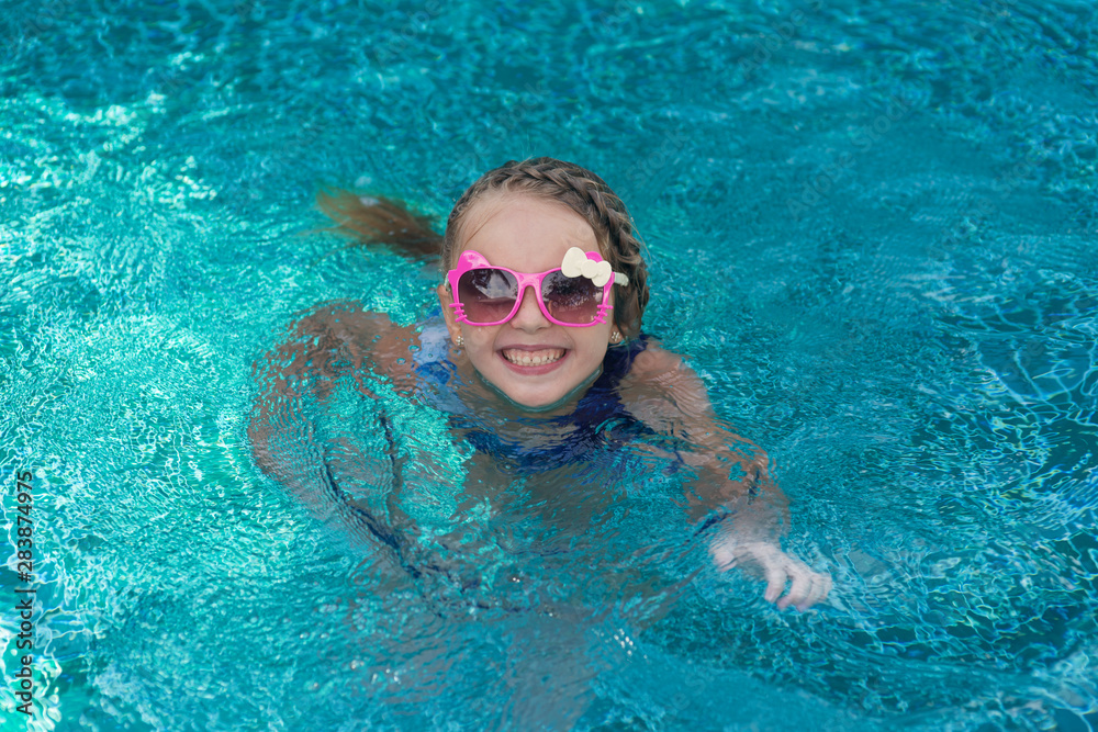 Naklejka premium Portrait of cute happy little girl having fun in swimming pool. Kids sport on family summer vacation. Active healthy holiday