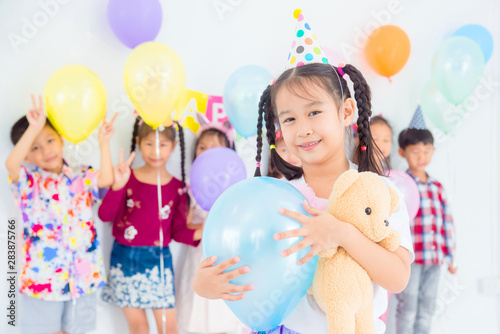 Little pretty girl holding blue balloon and smiles in birthday party with friends