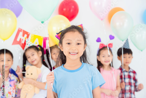 Little pretty girl holding green balloon and smiles in birthday party with friends