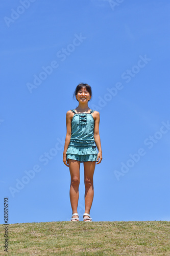 青空で笑う女の子（海水浴、水着、芝生広場）