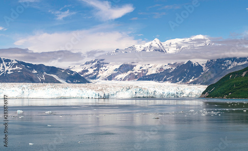 a section of the face of the hubbard glacier in yakutat bay in alaska with the st elias mountains and beautiful clouds in a blue sky in the background