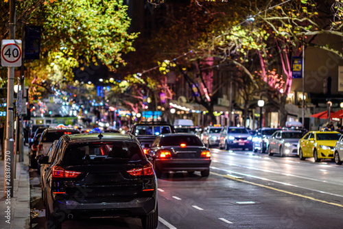 A downtown city street in Melbourne Australia at night, showing city lights, traffic and tram tracks