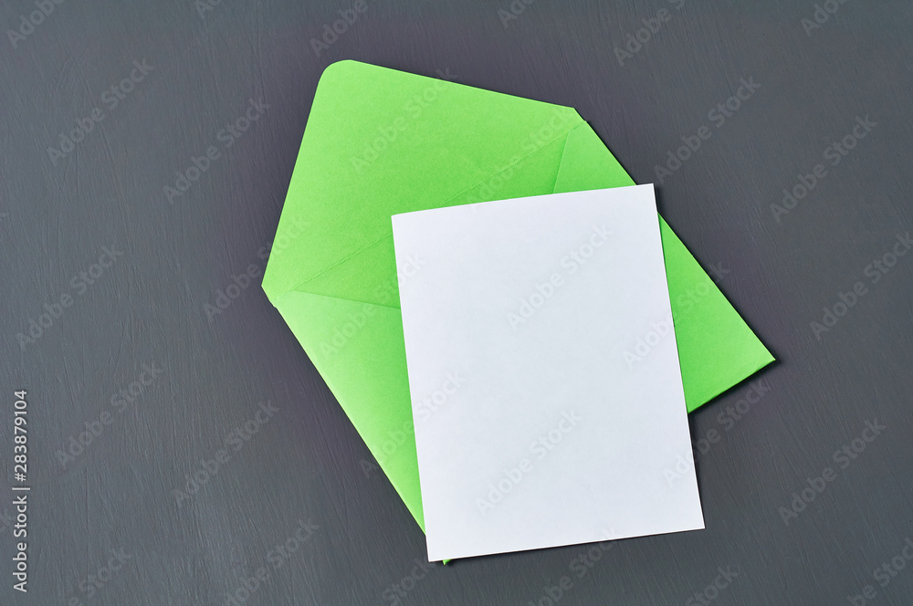 Blank white paper sheet near green opened square envelope lies on old scratched dark concrete. Space for text Blank white paper sheet near green opened square envelope lies on old scratched dark concrete. Space for text