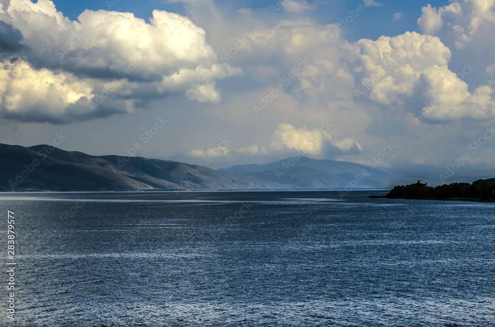 View of the sky, darkened by huge Cumulus clouds coming from the mountains and hanging over the mountain lake Sevan, located in the mountains of Armenia