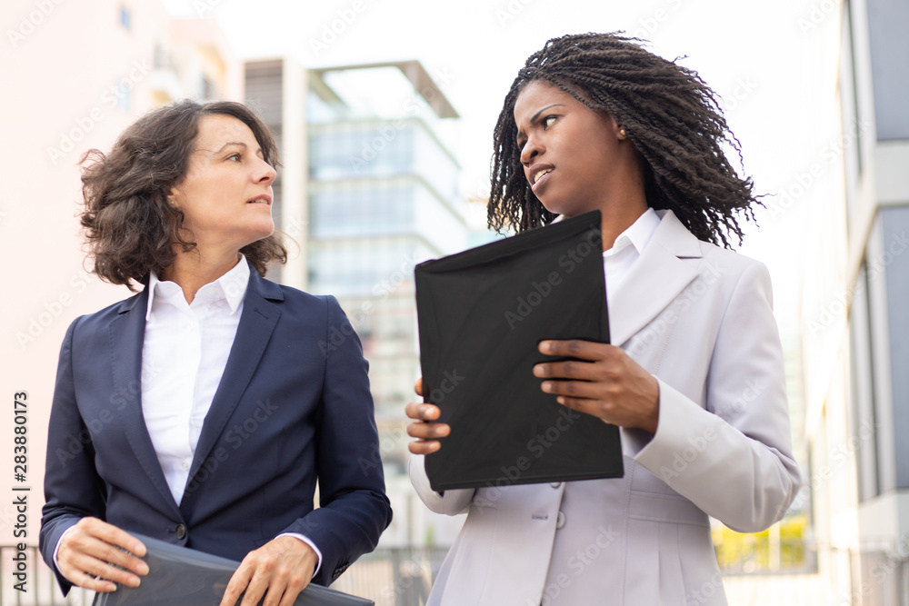Confident business consultants talking on street. Two cheerful businesswomen walking on street and talking. Business communication concept Confident business consultants talking on street. Two cheerful businesswomen walking on street and talking. Business communication concept
