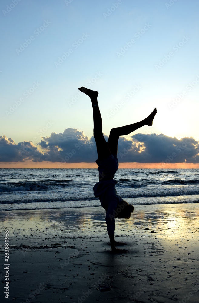 Junges Mädchen macht einen Handstand am Strand bei Sonnenaufgang - Silhouette im Gegenlicht