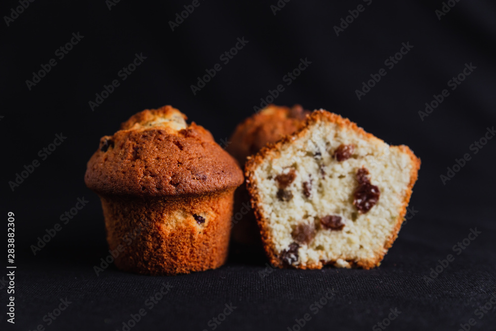 Muffins with raisins and one muffin cut in half on black background