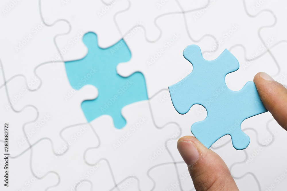 Human hand holding blue puzzle pieces over white puzzle grid background Human hand holding blue puzzle pieces over white puzzle grid background