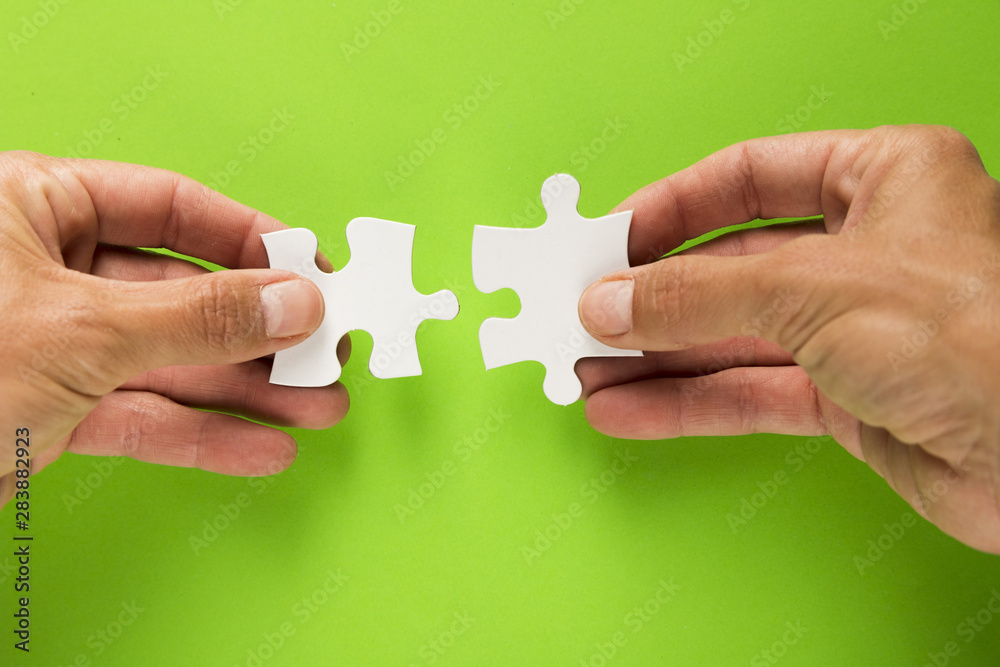 Close-up of male hand joining white jigsaw puzzle piece over green background Close-up of male hand joining white jigsaw puzzle piece over green background