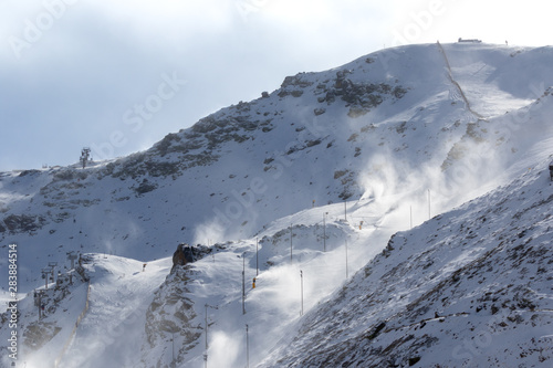 In the Spanish winter sports area Pradollano high in the Sierra Nevada. Cable car and chairlift in front of blue sky. The strong wind causes considerable snowdrifts in the air.