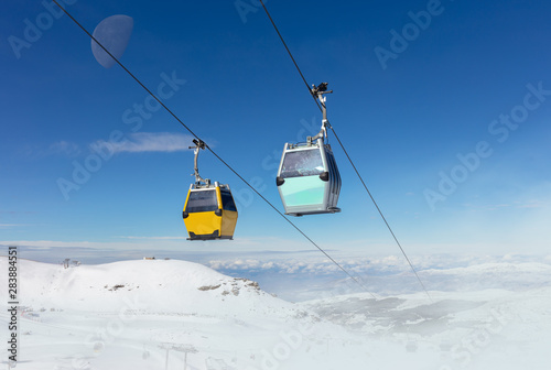 In the Spanish winter sports area Pradollano high in the Sierra Nevada. Cable car cabins in front of blue sky and snowdrifts in the air.