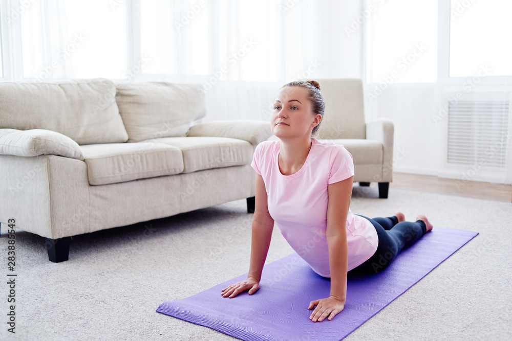 Portrait of young woman practicing yoga at home indoor, copy space. Girl practicing cobra pose, full length. Relaxing and doing yoga. Wellness and healthy lifestyle. Bhujangasana Portrait of young woman practicing yoga at home indoor, copy space. Girl practicing cobra pose, full length. Relaxing and doing yoga. Wellness and healthy lifestyle. Bhujangasana