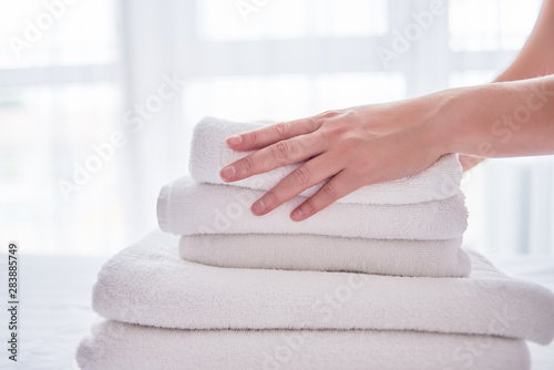 Woman putting stack of fresh white bath clean towels on bed sheet, copy space. Close up hands of hotel maid with towels. Room service
