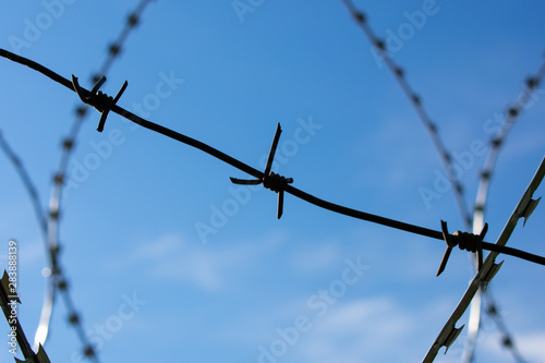 Barbed, rough, wavy wire against a bright blue sky with clouds. Restricted area. Protective wire. Egoza. photo