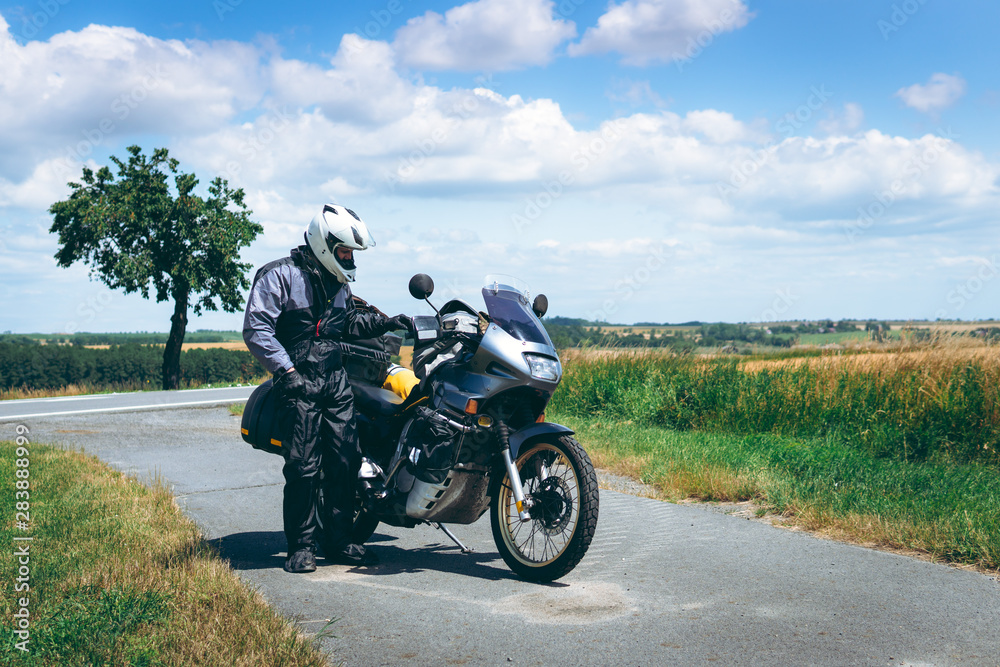 Obraz premium Mężczyzna kierowca w płaszczu przeciwdeszczowym stoi przy motocyklu przygodowym z bocznymi torbami. wycieczka motocyklowa. Na wolnym powietrzu. Świat podróż na dwóch kołach, koncepcja wolności. wyposażenie jeźdźca.