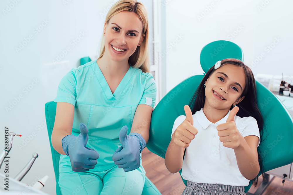Little girl and dentist showing thumbs up. successful teeth treatment
