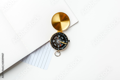 Black notepad for nautical notes and golden compass on a white table