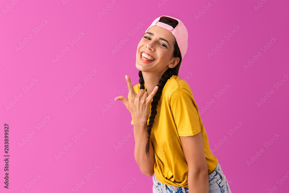 Photo of beautiful joyful woman wearing cap backwards smiling and showing rock sign Photo of beautiful joyful woman wearing cap backwards smiling and showing rock sign