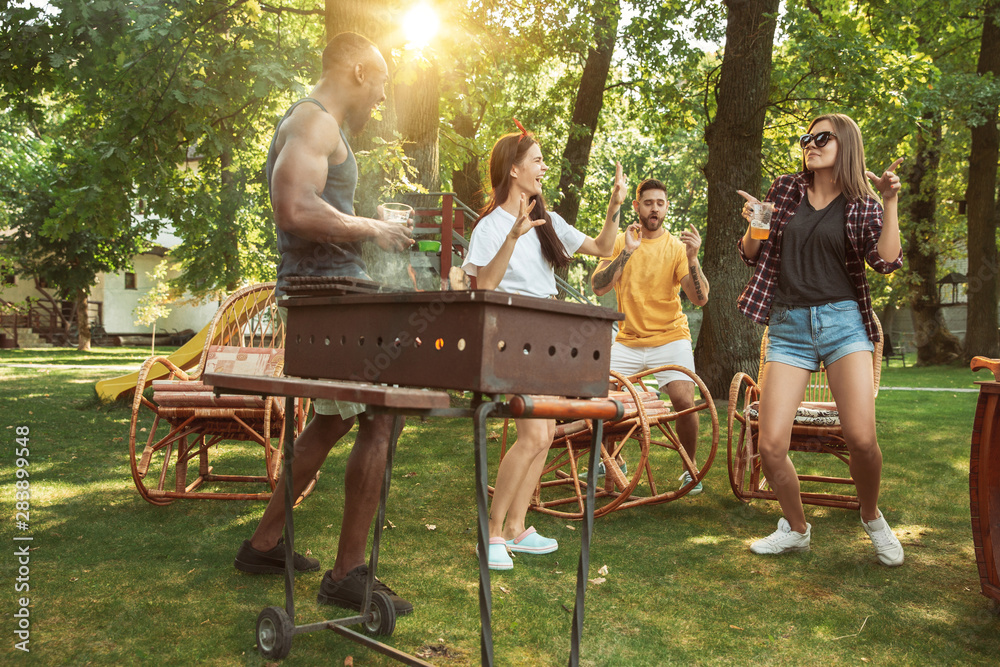 Group of happy friends having beer and barbecue party at sunny day. Resting together outdoor in a forest glade or backyard. Celebrating and relaxing, laughting. Summer lifestyle, friendship concept. Group of happy friends having beer and barbecue party at sunny day. Resting together outdoor in a forest glade or backyard. Celebrating and relaxing, laughting. Summer lifestyle, friendship concept.