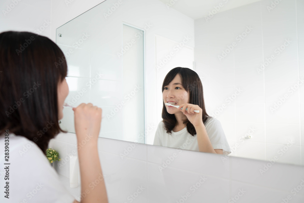 Young asian woman brushing her teeth in front of the bathroom mirror. Dental health care concept. Young asian woman brushing her teeth in front of the bathroom mirror. Dental health care concept.