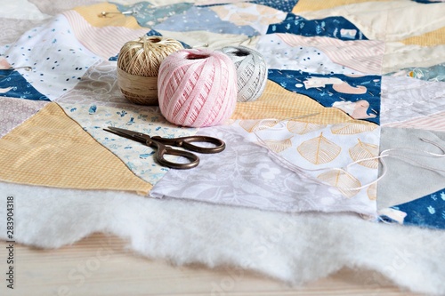 Hand stitch quilting process: cotton thread, needle and scissors on the table photo