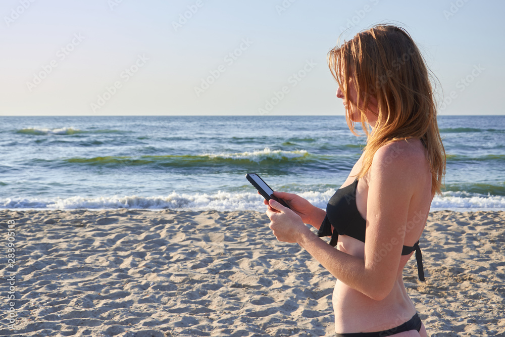 Cute smiling girl texting with her mobile phone message on a beach. Nice relax